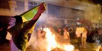 Manifestante abre a bandeira do Brasil em frente a fogueira durante confronto com a polícia, em Niterói  Foto: AFP