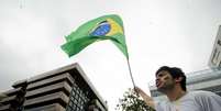 <p>Com bandeira do Brasil, manifestante faz coro a protesto na frente da casa de Cabral</p>  Foto: Mauro Pimentel / Terra