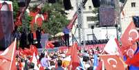 Premiê turco, ao fundo, fala em evento com simpatizantes neste sábado  Foto: Reuters