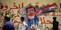 Manifestantes egípcios passam em frente a uma caricatura de Mursi pintada em uma parede do palácio presidencial, no Cairo  Foto: AFP