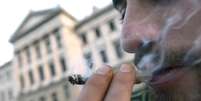 Homem fuma maconha do lado de fora do Congresso uruguaio, onde o projeto foi votado nesta quarta-feira  Foto: AP