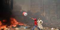 Manifestante joga galão d'água em fogo para tentar conter incêndio provocado pelos confrontos no Cairo  Foto: AFP
