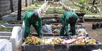 Funcionários de um cemitério da capital do Quênia colocam flores em uma das sepulturas  Foto: AFP