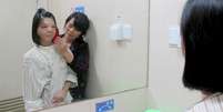 <p>Xu Jianmei se olha no espelho ao lado da mãe após ter a face reconstruída: cirurgia foi bem sucedida</p>  Foto: Reuters