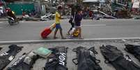 <p>Pessoas cobrem os narizes ao passarem por corpos enfileirados em Tacloban</p>  Foto: AP