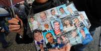 Mulher segura cartaz com fotos de amigos que teriam morrido de câncer durante protesto em Nápoles  Foto: AFP