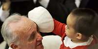 Criança brinca com o chapéu do Papa durante a audiência de sábado no Vaticano  Foto: AP