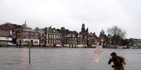 Mulher tenta se proteger do vento e da chuva em calçada alagada pelo rio Ouse em York, na Inglaterra  Foto: AP