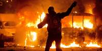 Manifestante atira pedra em ônibus da polícia em chamas   Foto: AP
