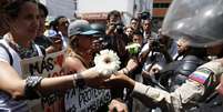 Manifestante de oposição dá flor a um policial durante protesto contra Nicolás Maduro  Foto: Reuters