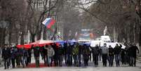 <p>Segurando uma bandeira russa, manifestantes marcham em frente ao prédio do governo, na Crimeia. De acordo com o Ministro do Interior ucraniano, a polícia está em alerta máximo depois que dezenas de manifestantes invadiram o edifício do Parlamento de Simferopol</p>  Foto: AP