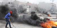 Manifestante líbio coloca fogo em pneus, bloqueando rua na capital do país, próximo ao Congresso  Foto: AFP