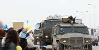 Um comboio militar russo passa por estrada em Simferopol, na Crimeia, neste sábado, enquanto manifestantes contra a guerra protestam  Foto: Reuters