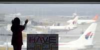 Menina observa os aviões, ao lado de uma placa que diz "temos esperanças", colocada no aeroporto internacional de Kuala Lumpur, na Malásia, nesta segunda-feira, 10 de março  Foto: AP