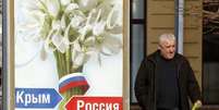 <p>Um homem passa na frente de um pôster com os dizeres "Crimeia - Rússia", em Simferopol</p>  Foto: Vasily Fedosenko / Reuters