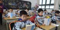 <p>Alunos lêem livros em mesas equipadas com o objetivo de prevenir a miopia, em uma escola primária em Wuhan, província de Hubei, China, em 10 de março</p>  Foto: Reuters