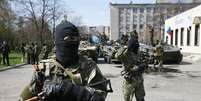 <p>Homens armados, usando fitas pretas e laranja de St. George - símbolo amplamente associado com os protestos pró-russos no país, montam guarda em frente a veículos blindados em Slaviansk, na Ucrânia, em 16 de abril</p>  Foto: Reuters