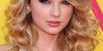 A cantora Taylor Swift usa cachos largos com franjão jogado para o lado   Foto: Shutterstock