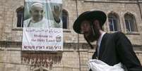 <p>Judeu ultra-ortodoxo é visto passando em frente de um cartaz em homenagem ao Papa, na Velha Jerusalém</p>  Foto: Reuters