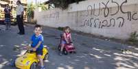 <p>Crianças brincam em frente ao muro pichado com as palavras "árabes fora" e "racismo ou assimilação", no povoado árabe israelense de Abu Ghosh, em 18 de junho</p>  Foto: AFP