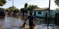 <p>Homem caminha com dois cachorros em uma rua totalmente alagada em Assun&ccedil;&atilde;o</p>  Foto: Reuters