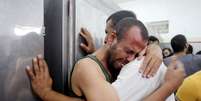 Palestinos choram após encontrarem nome de familiar entre os mortos em bombardeio israelense  Foto: Ibraheem Abu Mustafa / Reuters