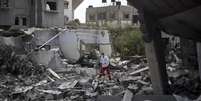 <p>Palestinos caminham entre prédios bombardeados em bairro de Gaza</p>  Foto: Mahmud Hams / AFP