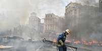 <p>Um bombeiro extingue um incêndio causado pela queima de uma barricada na Praça da Independência, em Kiev, durante confrontos de residentes da capital ucraniana, neste sábado, 9 de agosto</p>  Foto: SERGEI SUPINSKY / AFP