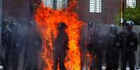 Um policial é incendiado por um coquetel molotov lançado por um pequeno grupo de manifestantes durante confrontos em San Cristobal, na Venezuela  Foto: GEORGE CASTELLANOS / AFP