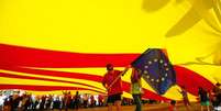 <p>Manifestantes carregam&nbsp;bandeira da Uni&atilde;o Europeia sob uma bandeira gigante da Catalunha durante protesto em Barcelona, no Dia Nacional da Espanha</p>  Foto: Albert Gea / Reuters