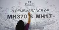 <p>Mulher escreve em painel de mensagem em homenagem a vítimas de voos da Malaysia Arilines MH370 e MH17, em Subang Jaya, em 23 de julho</p>  Foto: Samsul Said / Reuters