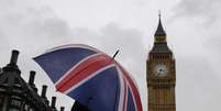 <p>Uma mulher com guarda-chuva nas cores da bandeira do Reino Unido à frente do Big Ben</p>  Foto: Luke MacGregor / Reuters