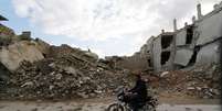 Homem conduz sua motocicleta em frente a escombros de prédios em Maaret al-Naaman, na província de Idlib, Síria. 27/11/2014.  Foto: Khalil Ashawi / Reuters