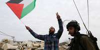 Manifestante palestino exibe bandeira palestina ao lado de um soldado israelense, durante protesto contra assentamentos judeus em Maasara, perto de Bel&eacute;m, na Cisjord&acirc;nia, em dezembro. 19/12/2014  Foto:  Mussa Qawasma / Reuters