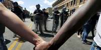 Membros da comunidade dão as mãos em frente a tropas de choque em Baltimore, nos Estados Unidos, nesta terça-feira. 28/04/2015  Foto: Jim Bourg / Reuters