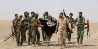 Paramilitares xiitas iraquianos e soldados iraquianos seguram bandeira do Estado Islâmico  Foto: Stringer / Reuters