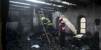 Bombeiros israelenses trabalham em meio aos destroços causados por um incêndio na igreja onde Jesus Cristo fez o milagre da multiplicação de pães e peixes  Foto: Baz Ratner / Reuters