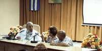 Ex-presidente de Cuba aparece vestido com uma jaqueta branca esportiva e camisa quadriculada, sentado na cabeceira de uma sala de reuniões e acompanhado de dois funcionários cubanos  Foto: Estudios Revolución / EFE