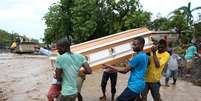 Homens carregam caix&atilde;o e tentam atravessar o rio La Digue ap&oacute;s a derrubada da &uacute;nica ponte pelo furac&atilde;o Matthew  Foto: EFE