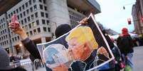 Homem protesta contra Donald Trump segurando cartaz do presidente eleito beijando Putin  Foto: Getty Images