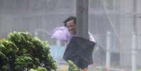 Homem se segura em poste durante fortes ventos causados pelo tufão em Hong Kong  Foto: Reuters
