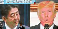 Homem passa diante de telão com as imagens do premiê japonês, Shinzo Abe, e do presidente dos EUA, Donald Trump, em Tóquio  Foto: Reuters