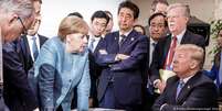 Angela Merkel (c., de pé) diante de Donald Trump na mesa de negociações do G7  Foto: DW / Deutsche Welle