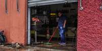 Homem limpa sujeira levada pela enchente no bairro do Cambuci, em São Paulo  Foto: Ananda Migliano/O Fotográfico / Estadão