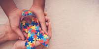 Mãos que prendem a fita do enigma para a consciência do autismo   Foto: iStock