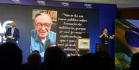 Eduardo Bolsonaro fala no palco, com imagem e frase de Olavo de Carvalho na tela atrás; em primeira edição de evento conservador no Brasil, o deputado foi ovacionado pela plateia  Foto: Ligia Guimarães/BBC / BBC News Brasil