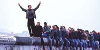 Alemães ocidentais celebram o colapso do comunismo no topo do Muro de Berlim, em 12 de novembro de 1989  Foto: Getty Images / BBC News Brasil