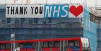 A Docklands Light Railway train is seen passing a banner on a construction site thanking the NHS, as the spread of the coronavirus disease (COVID-19) continues, London, Britain, April 8, 2020. REUTERS/Andrew Couldridge - RC2F0G9HPIV2  Foto: Reuters