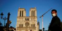 Homem com máscara de proteção passa pela frente da catedral de Notre-Dame de Paris, enquanto o sino tocava. 15/4/2020. REUTERS/Gonzalo Fuentes  Foto: Reuters