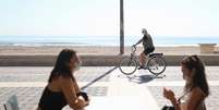 Mulheres com máscaras de proteção conversam em restaurante na beira da praia enquanto homem anda de bicicleta em Valência
18/05/2020 REUTERS/Nacho Doce  Foto: Reuters